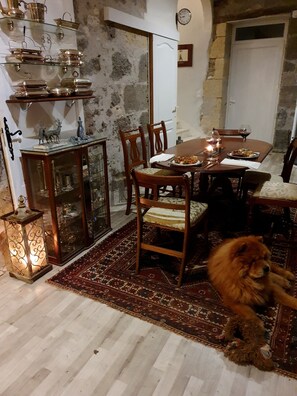 A dining area with a round table, chairs, a rug, a dog, and a wall with a clock. - Chambre Lavande aux Quatre Vents with Shared Terrace and Garden (Francescas)