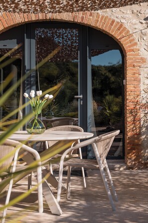 Eine Terrasse im Freien mit einem runden Tisch und Stühlen, einer Vase mit Blumen sowie einer Ziegelwand.