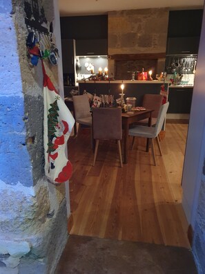 Un coin repas avec une table et des chaises en bois, une nappe aux motifs de Noël, et une cuisine en arrière-plan.