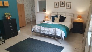A bedroom with a metal bed frame, a dark rug, a wooden dresser, a small window, and wall-mounted artwork. - Holiday Home Les Quatre Vents with Shared Garden, Terraces, Wi-Fi, and Air Conditioning (Francescas)