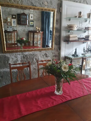 Un comedor con una mesa dispuesta para dos personas, un florero con flores, un espejo y un aparador con vajilla.