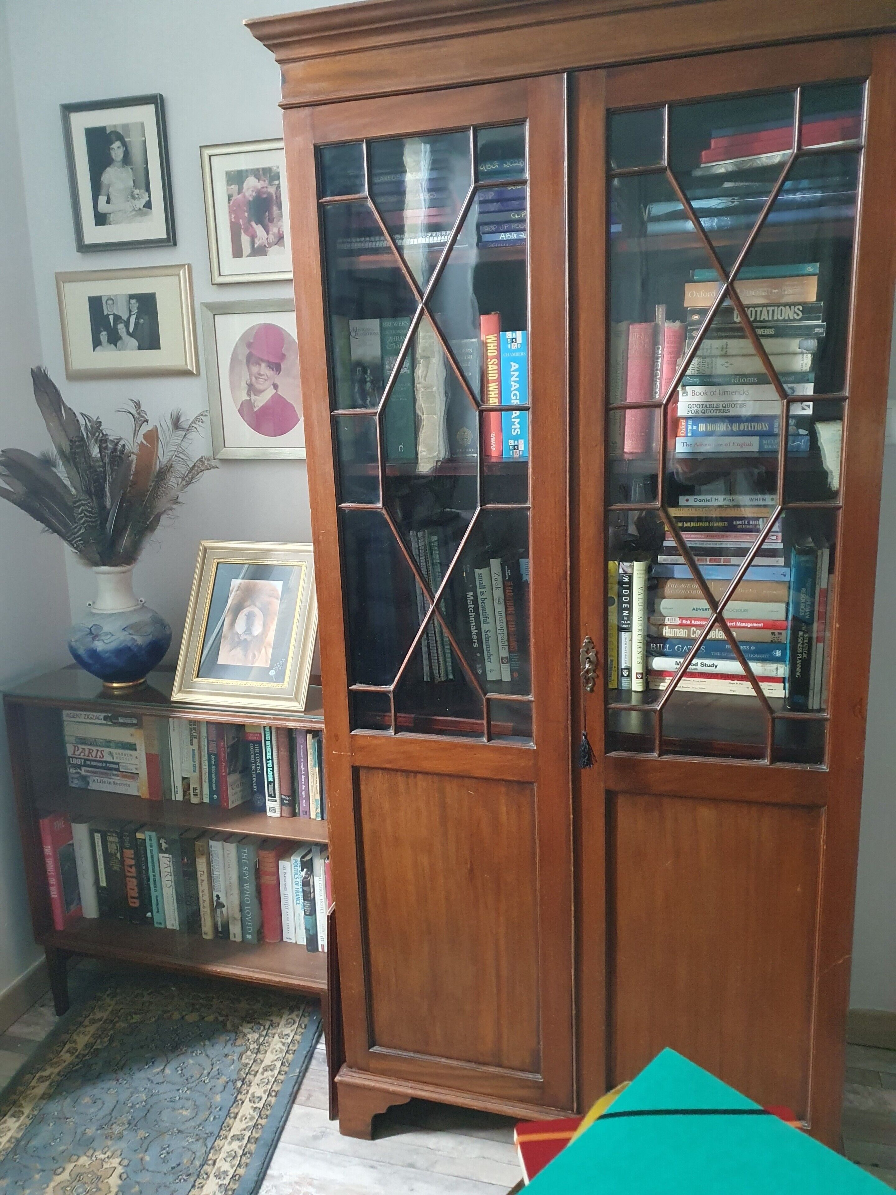 A wooden bookcase with glass doors, a framed picture, and a vase with dried plants.