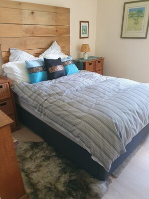 Quarto com cabeceira de madeira, cama com roupa de cama listrada, mesa de cabeceira com abajur e um quadro na parede.
