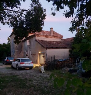 Uma casa rústica com telhado de telhas, um carro estacionado em frente e uma área de jardim.