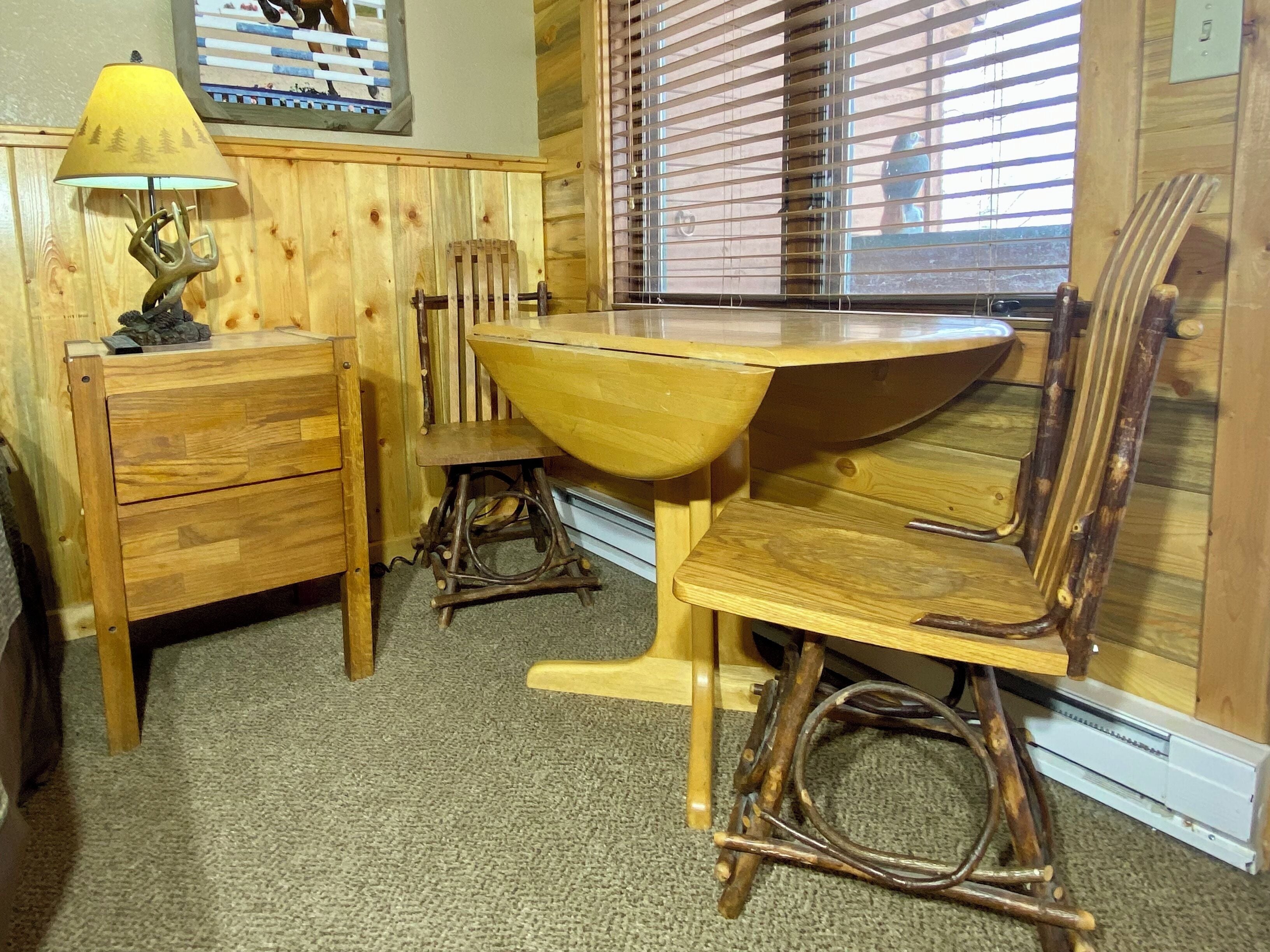 Una mesa de comedor de madera con sillas, una lámpara y un cuadro en la pared.