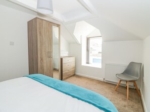 Une chambre à coucher comprenant un lit, une armoire, une chaise, une fenêtre et un radiateur.