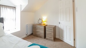 Une chambre à coucher comprenant un lit, une commode, un miroir, une lampe, un radiateur et une porte.