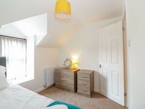 Ein Schlafzimmer mit einem Bett, einem Schminktisch, einem Spiegel, einer Lampe, einer Heizung und einer Tür.