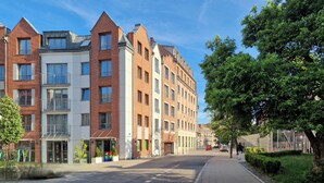 Une rangée d’immeubles modernes à plusieurs étages, avec un trottoir pavé et une rue bordée d’arbres.