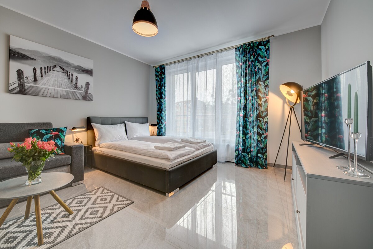 A modern bedroom with a bed, a sofa, a TV, and a painting on the wall.