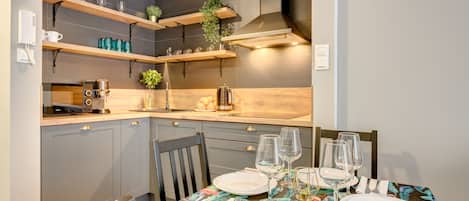 A modern kitchen with built-in appliances, wooden shelves, and a dining table set for four.