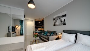 Une chambre d’hôtel moderne avec un lit, un canapé, un coin repas et une cuisine en arrière-plan.