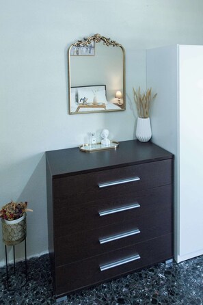 Eine dunkelbraune Kommode mit Schubladen, ein Spiegel mit dekorativem Rahmen und eine Vase mit Trockenpflanzen.
