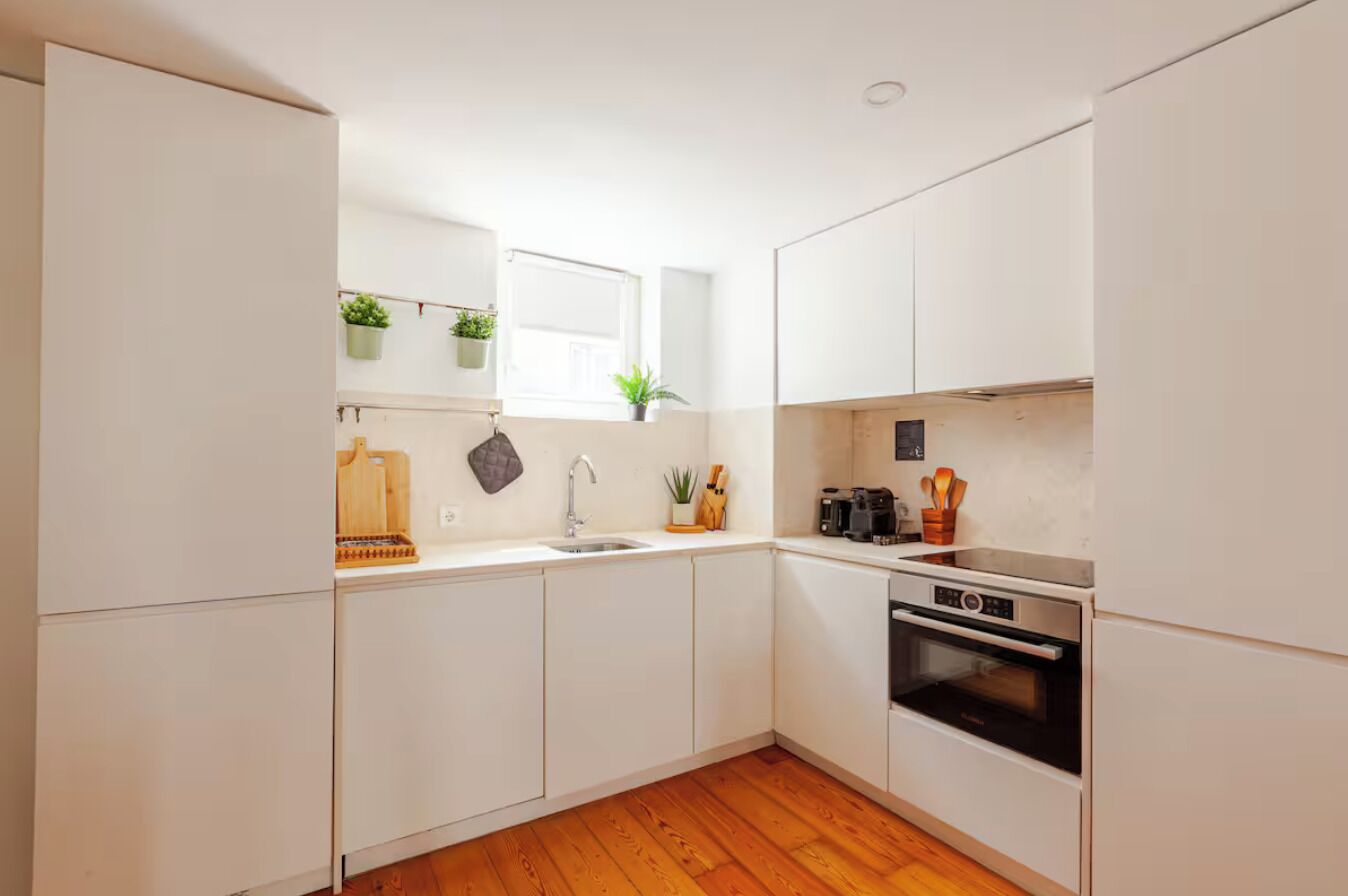 A compact kitchen with white cabinets, a wooden countertop, a sink, a stove, and a window with plants.
