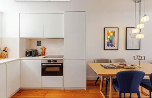 Eine moderne Küche mit weißen Schränken, einem eingebauten Backofen und einem Essbereich mit Tisch und Stühlen.