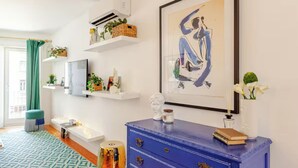 A modern living room with a blue dresser, a framed abstract painting, and a television on a white stand. - Stylish Retreat with Rare Rooftop Pool | 2BR, 2BA (Lisboa)