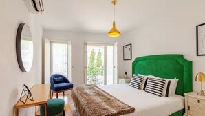 A bedroom with a bed, a desk, a chair, a bedside table, and a hanging light fixture. - Stylish Retreat with Rare Rooftop Pool | 2BR, 2BA (Lisboa)