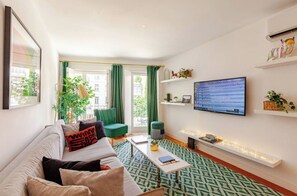 Ein modernes Wohnzimmer mit einer Couch, einem Couchtisch, einem Fernseher und einem gemusterten Teppich in Grün.
