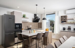 A modern kitchen with a refrigerator, microwave, and stove, bar stools, and a large window. - Luxurious home in Krnica (Krnica)