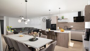 Eine moderne Küche mit Essbereich, ausgestattet mit einer zentralen Kochinsel, Pendelleuchten und einem eingebauten Backofen.