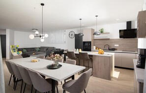 A modern kitchen with a dining area, featuring a central island, pendant lighting, and a built-in oven. - Luxurious home in Krnica (Krnica)