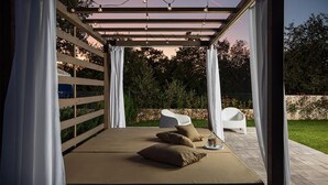 Ein überdachter Außenbereich mit Pergola, Kissen und einer Flasche auf einem Tablett.