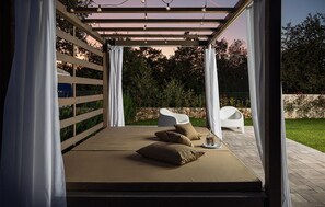 A covered outdoor seating area with a pergola, cushions, and a bottle on a tray. - Luxurious home in Krnica (Krnica)