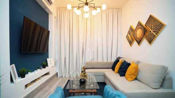 Ein Wohnzimmer mit einer Couch, einem Couchtisch, einem an der Wand befestigten Fernseher und einem Fenster mit Vorhängen.