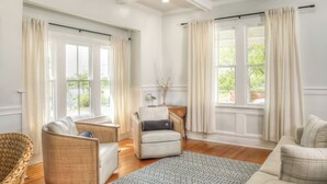 A spacious living room with a large window, a wicker chair, a sofa, and a patterned rug. - Modern Downtown Living with Panoramic River Views (Wilmington)