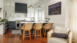 A modern kitchen with white cabinets, a central island, and bar stools. - Modern Downtown Living with Panoramic River Views (Wilmington)