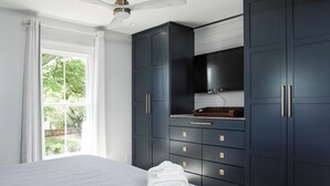 A bedroom with a bed, a TV, and dark blue cabinets. - Modern Downtown Living with Panoramic River Views (Wilmington)