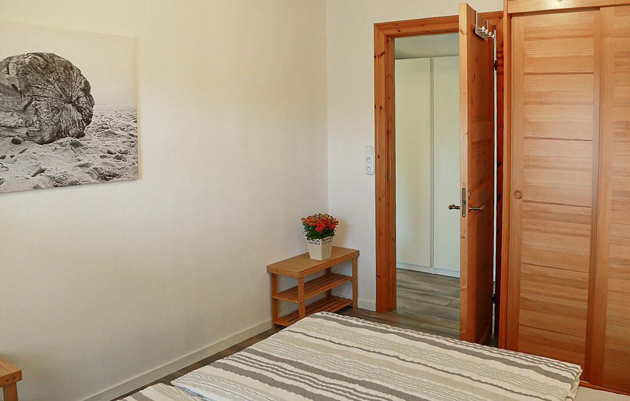 Ein Schlafzimmer mit einem Bett, einer Holztür, einem kleinen Tisch mit Pflanze und einem an der Wand hängenden Bild.