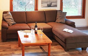 Ein braunes Ecksofa mit Couchtisch aus Holz, zwei Weingläser, eine Weinflasche und ein Buch auf der rechten Seite.