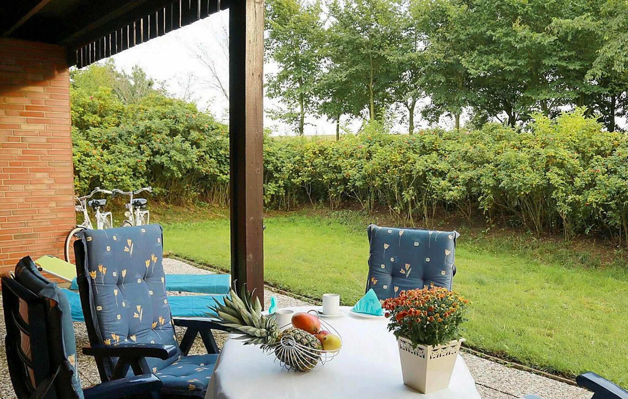 Eine Terrasse im Freien mit zwei blauen Stühlen, einem Tisch mit Früchten und einem Blumentopf, sowie einem Fahrrad im Hintergrund.