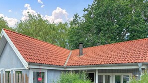 Ein Haus mit rotem Ziegeldach, Schornstein und einer Veranda mit hängenden Pflanzen.