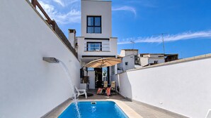 Ein Schwimmbecken, in das Wasser fließt, umgeben von einem weißen Gebäude mit einem Balkon und einem Fenster.