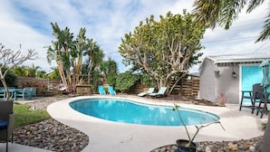 A swimming pool with lounge chairs, surrounded by trees and a small garden area. - Space Coast Retreat With Heated Pool (Merritt Island)
