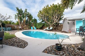 Ein Schwimmbecken mit Liegestühlen, umgeben von Bäumen und einer kleinen Gartenanlage.