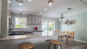 A kitchen with a large island, bar stools, wooden chairs, and a dining table. - Space Coast Retreat With Heated Pool (Merritt Island)