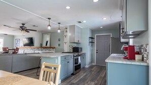 A modern kitchen with a central island, built-in appliances, and a dining area with a wooden table and chairs. - Space Coast Retreat With Heated Pool (Merritt Island)