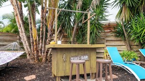 A wooden bar area with stools, a hammock, and a blue lounge chair. - Space Coast Retreat With Heated Pool (Merritt Island)