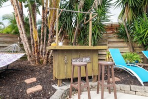 Eine Bar mit Holztresen, Hocker, einer Hängematte und einem blauen Liegestuhl.