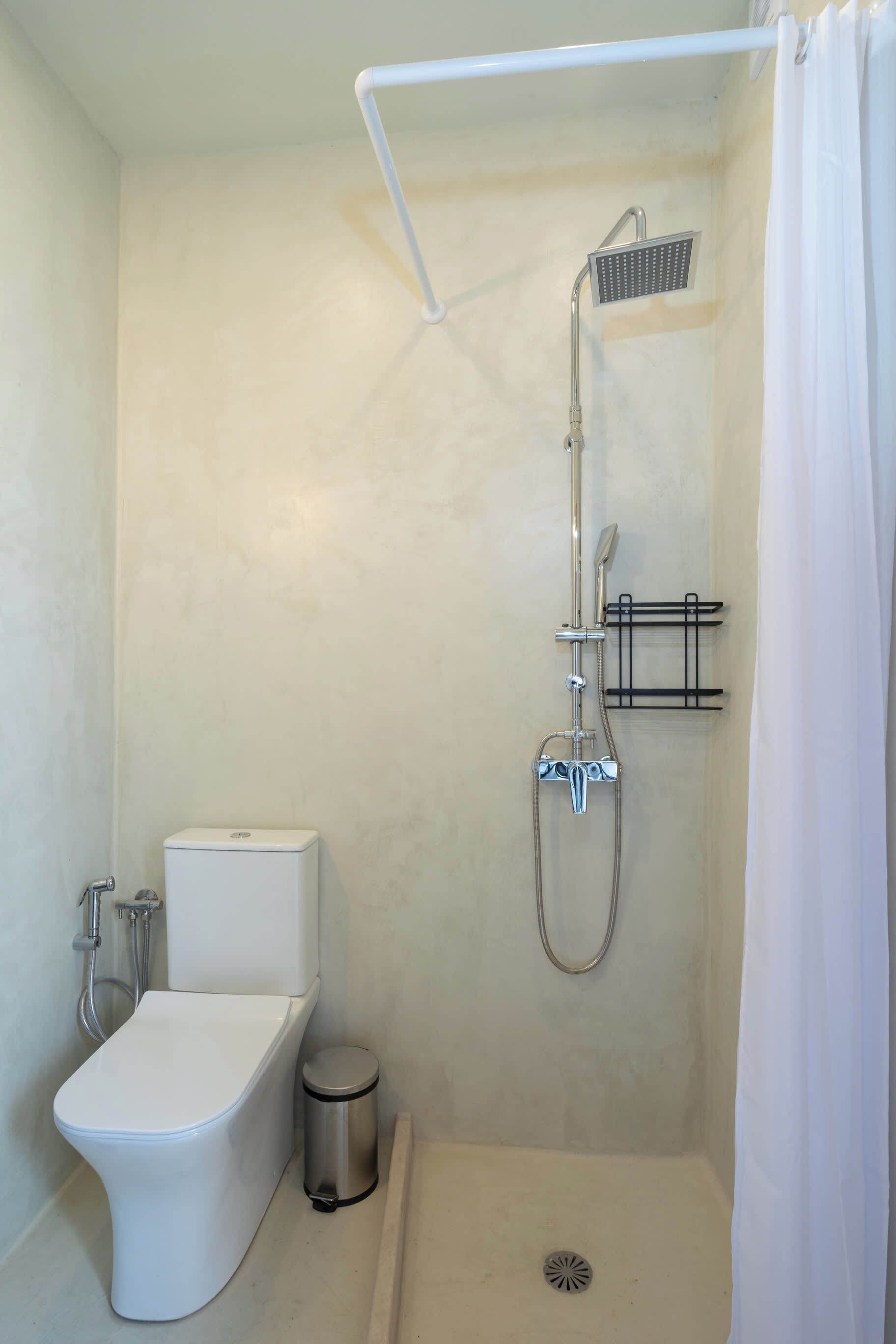 Een badkamer met een douche, toilet en prullenbak.