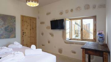 A bedroom with a bed, towels, a television, a window, and a stone wall.