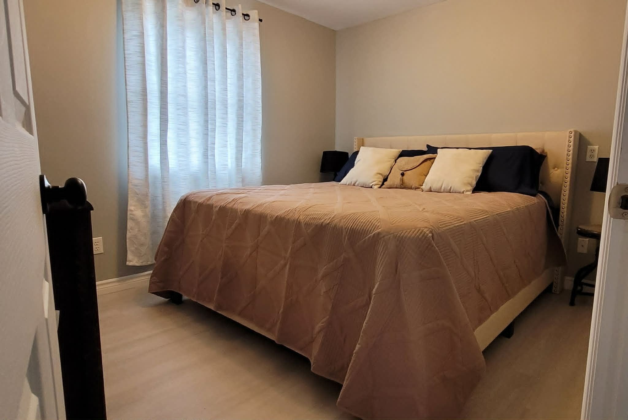 Un dormitorio con cama, cortinas, una mesita de noche y una silla.