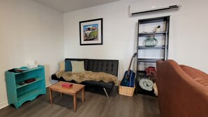 Ein Wohnzimmer mit einer Couch, einem Couchtisch, einem Bücherregal, einer Gitarre und einer Wandklimaanlage.