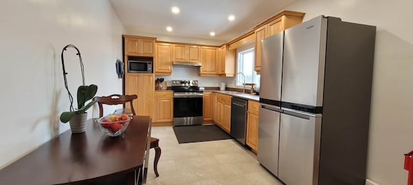 A compact kitchen with wooden cabinets, a stainless steel refrigerator, a microwave, and a stove.