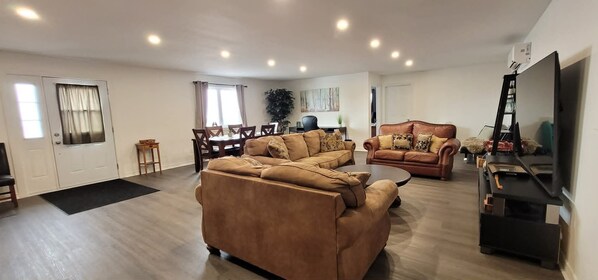 A spacious living area with a sofa set, a dining table, and a flat-screen TV.