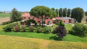 Ein großes Gebäude mit rotem Dach, umgeben von einem gepflegten Garten mit Sträuchern und einer Rasenfläche.
