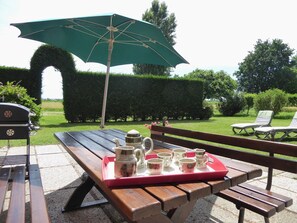 Eine Terrassenausstattung mit Holztisch, grünem Sonnenschirm und Grill.
